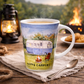 Ceramic mug with 'Happy Campers' design on a wooden table with a campfire and lantern in the background.