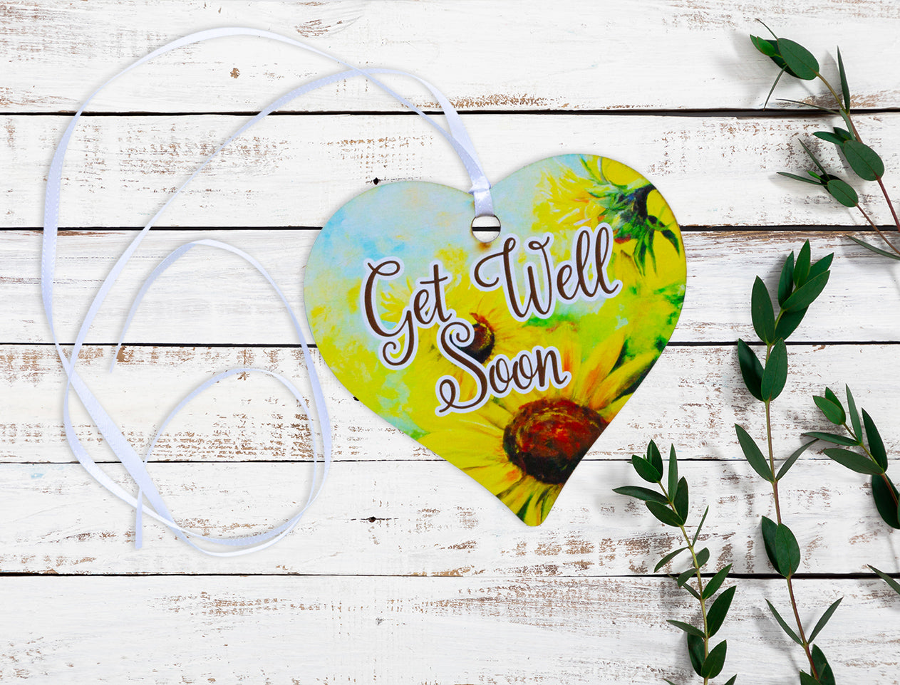 A wooden heart gift tag with a daisy illustration and get well soon message written on across the middle.