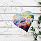 A wooden heart with have a happy day written on and a floral design.