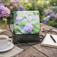 Floral-patterned handbag on a wooden table with coffee, notebook, and glasses.