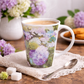 Mug with floral design on a wooden table with flowers and cookies in the background