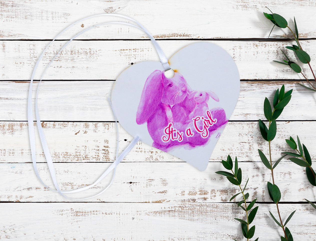 A wooden heart gift tag with a pink bunny illustration and written message of It's a Girl.