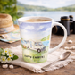 Mug with 'Happy Campers' design featuring a camper van, placed on a wooden surface with a scenic background.