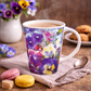 Floral-patterned mug with steaming coffee on a wooden table with cookies and macarons.