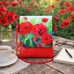 Floral-patterned red bag on a wooden table with coffee, notebook, and glasses.