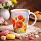 Colorful floral mug with steaming coffee on a wooden table with cookies and flowers.